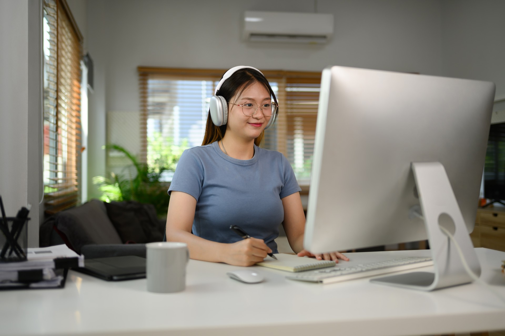 Charming Asian woman wearing headphone working on desktop computer at home