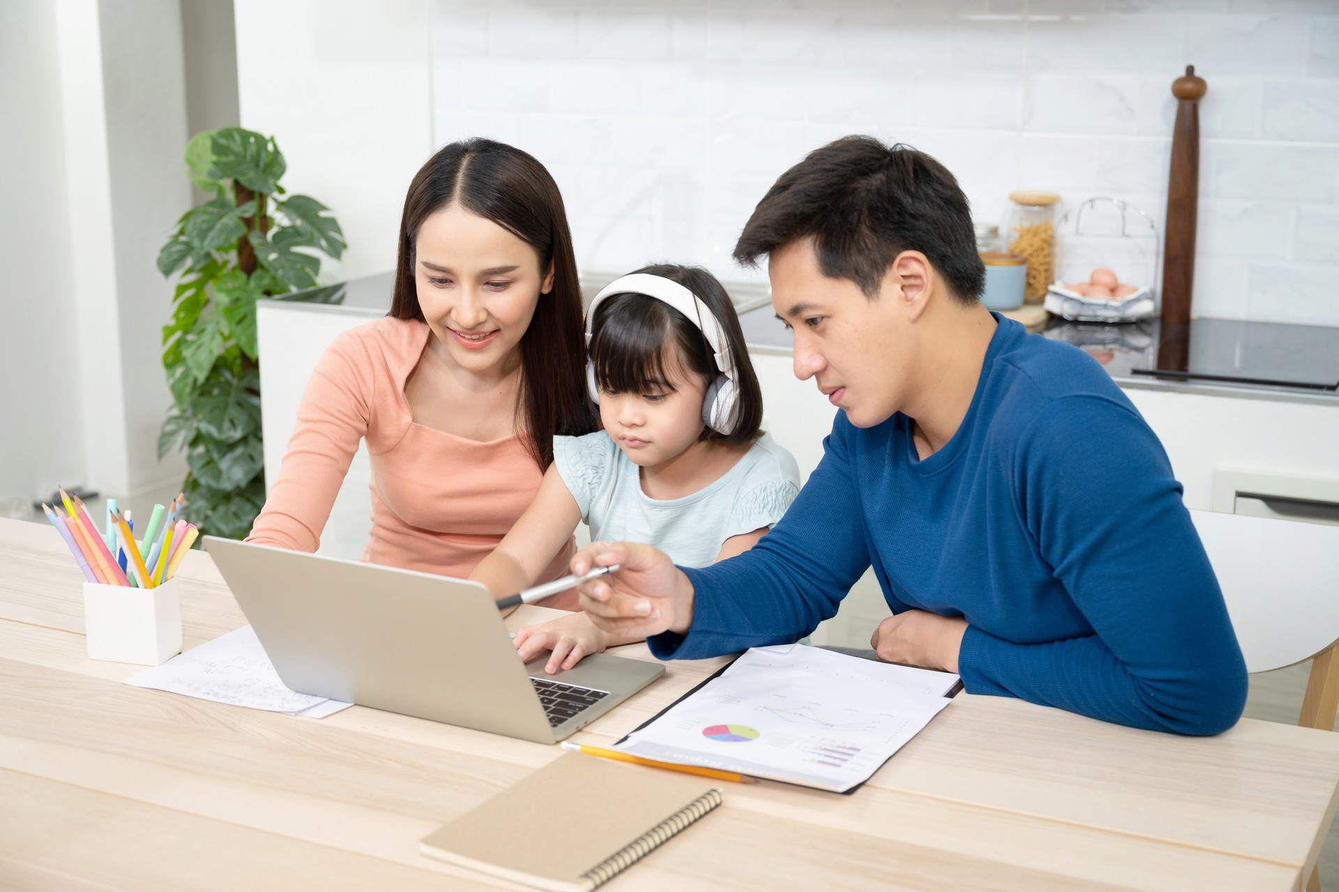 Asian father, mother and daughter doing home work together in living room, education at home and family concept